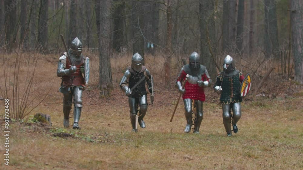 Four men knightes running in the row in the forest in full armour holding weapons Four men knightes running in the row in the forest in full armour holding weapons