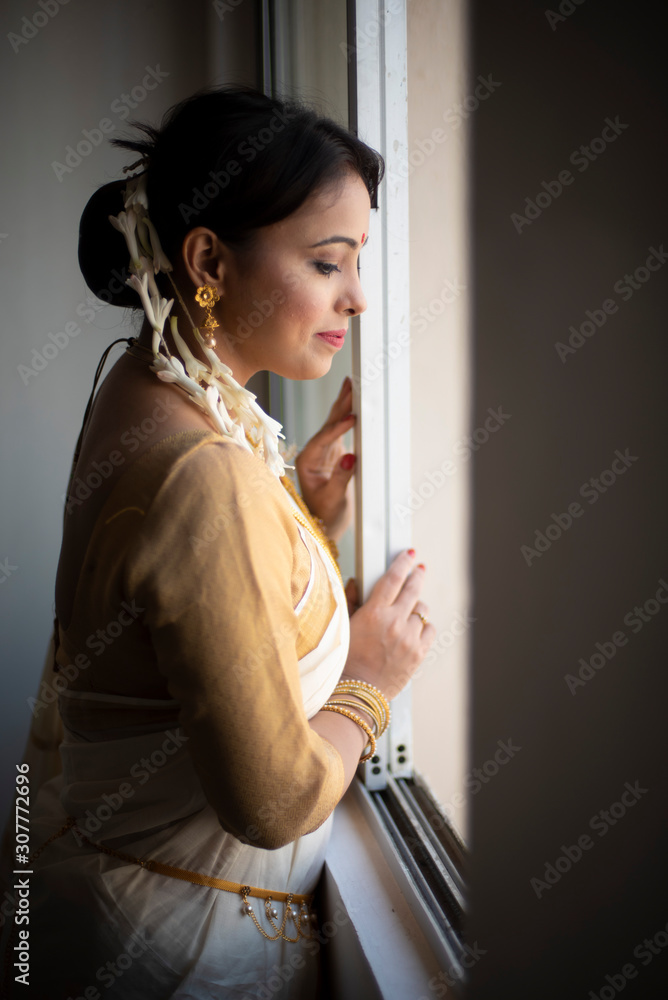 Portrait of an young and attractive Indian  woman in white traditional wear getting ready for the celebration of Onam/Pongal in white background. Indian lifestyle.