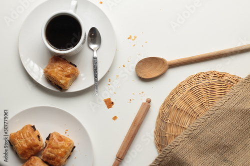 Flat lay of fresh, relaxed setting of black coffee and Pan Au Chocolate French inspired afternoon tea arrangement with clean white background with copy space and timber and brown accents and textures