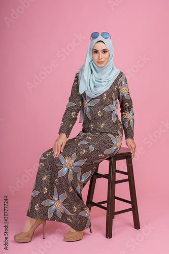 Beautiful female model wearing batik design  baju kurung  with light green hijab  sitting in various poses isolated over pink background. Eidul fitri fashion and beauty concept.