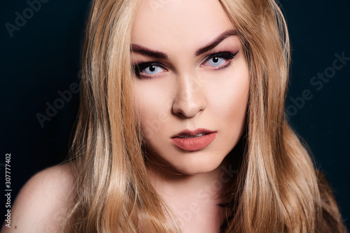 Blonde with long hair looking at the camera. Professional makeup, beautiful eyebrows, white lenses. Looking vampires, bright eyes. Hair care. Blindinka on a black back