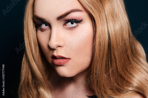 Blonde with long hair looking at the camera. Professional makeup, beautiful eyebrows, white lenses. Looking vampires, bright eyes. Hair care. Blindinka on a black back