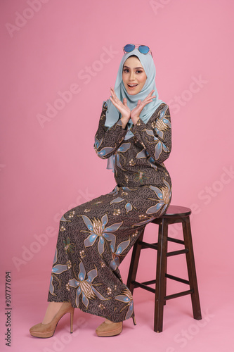Beautiful female model wearing batik design  baju kurung  with light green hijab  sitting in various poses isolated over pink background. Eidul fitri fashion and beauty concept.