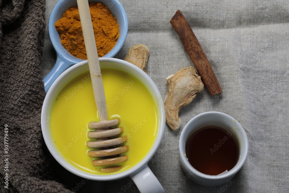 Turmeric latte, golden milk or the anti-inflammatory Indian Haldi Doodh with superfood Turmeric powder, Ginder and Cinnamon sweetened with honey on wooden background Turmeric latte, golden milk or the anti-inflammatory Indian Haldi Doodh with superfood Turmeric powder, Ginder and Cinnamon sweetened with honey on wooden background