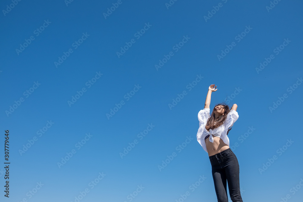 Happy woman with tanned slim body breathing fresh air raising her arms up, enjoying a sunny summer holiday on beach destination against blue sky, outdoors. Travel and well being lifestyle. Happy woman with tanned slim body breathing fresh air raising her arms up, enjoying a sunny summer holiday on beach destination against blue sky, outdoors. Travel and well being lifestyle.