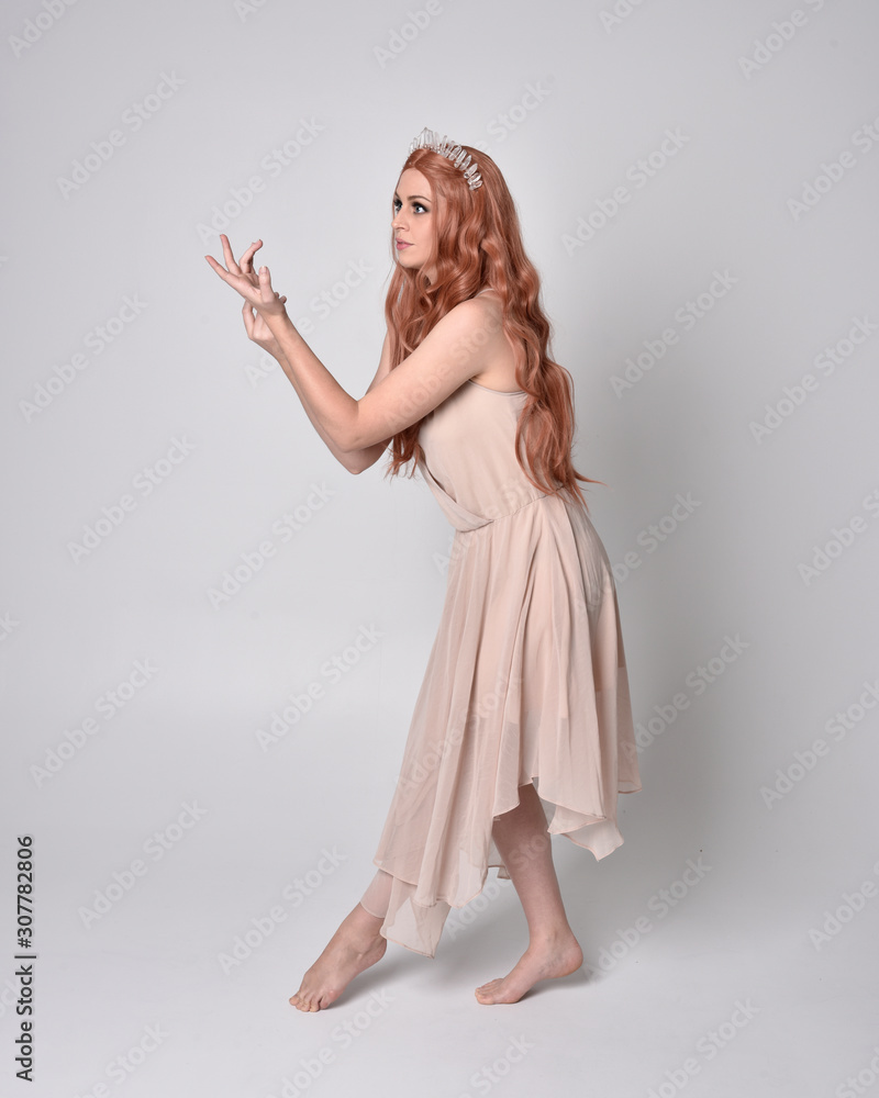 full length portrait of a pretty, fairy girl wearing a nude flowy dress and crystal crown. Standing and dancing pose against a grey studio background. full length portrait of a pretty, fairy girl wearing a nude flowy dress and crystal crown. Standing and dancing pose against a grey studio background.