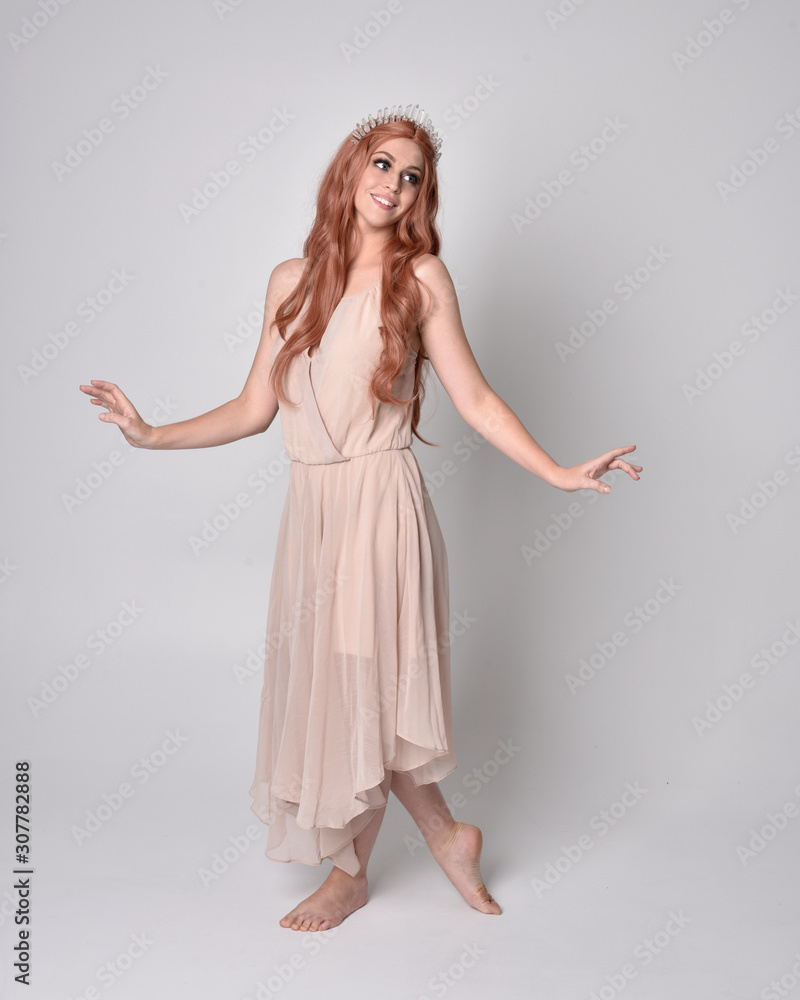 full length portrait of a pretty, fairy girl wearing a nude flowy dress and crystal crown. Standing and dancing pose against a grey studio background. full length portrait of a pretty, fairy girl wearing a nude flowy dress and crystal crown. Standing and dancing pose against a grey studio background.