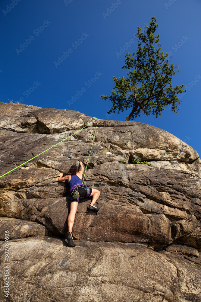Adventurous Girl is Rock Climbing up a Steep Cliff during a summer sunset. Taken in Lighthouse Park, West Vancouver, British Columbia, Canada.