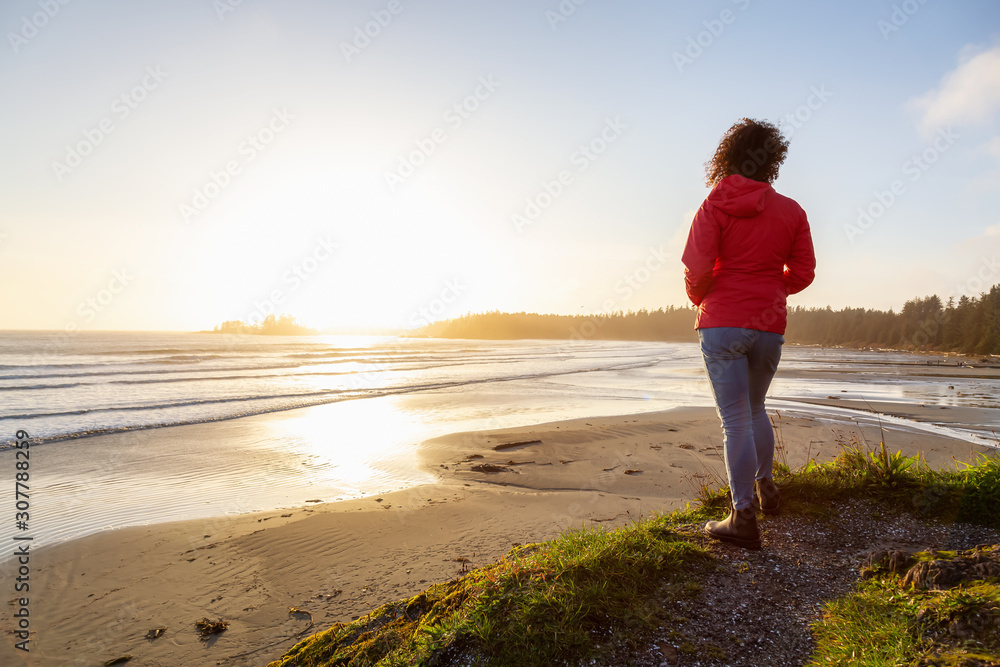 Long Beach, Near Tofino and Ucluelet in Vancouver Island, BC, Canada. Adventurous Girl standing and watching the golden sunset on the Pacific Ocean Coast.