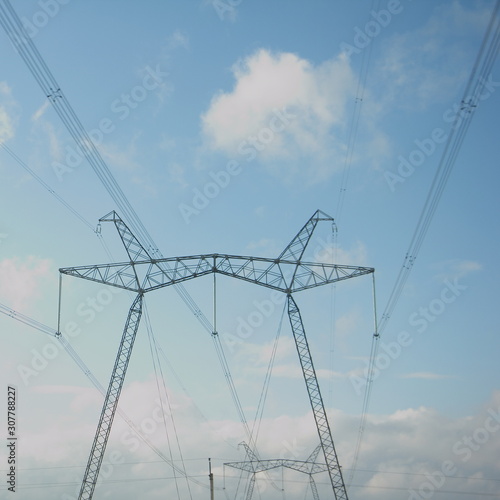 Close up mast of an air power line, electricity pylon with wires and insulators on blue sky with cloud background - traditional energy, electric power