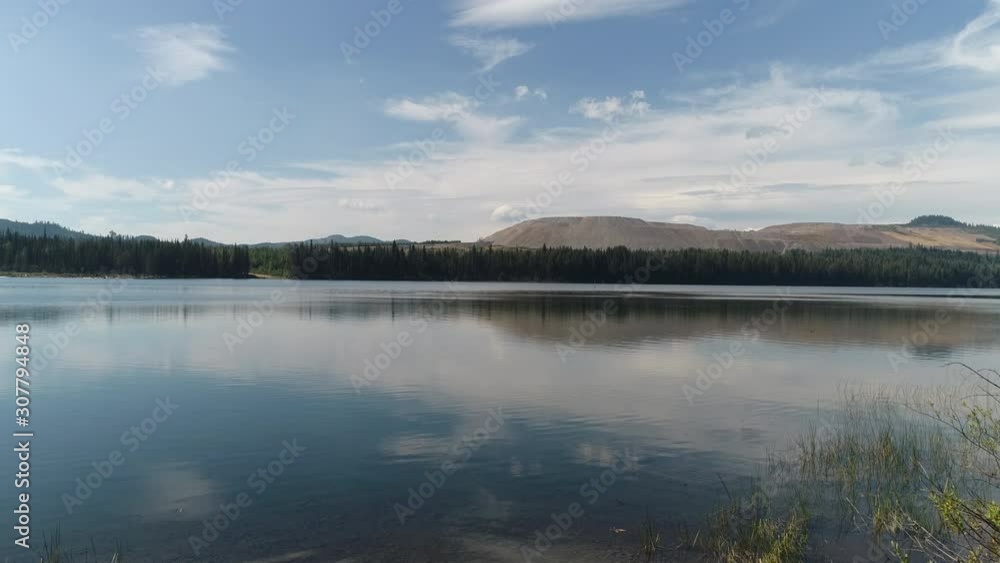 Drone, aerial, wide shot of a beautiful lake, camera then rises to show the trees and mountains beyond the lake. Drone, aerial, wide shot of a beautiful lake, camera then rises to show the trees and mountains beyond the lake.