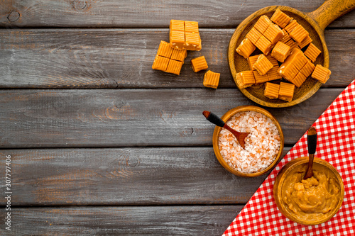 Prepare salted caramel. Scoop with sweet cubes, melted caramel and salt on dark wooden background top view copy space photo