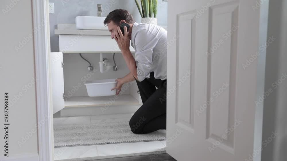 Man At Home Calling and Mopping Up Water From Leaking Pipe In Bathroom Man At Home Calling and Mopping Up Water From Leaking Pipe In Bathroom