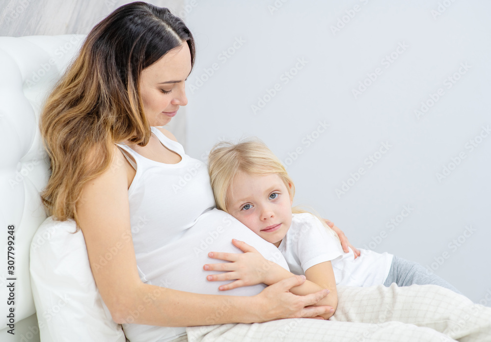 A pregnant woman with her little daughter on the bed A pregnant woman with her little daughter on the bed