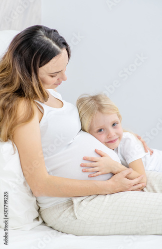 A pregnant woman with her little daughter on the bed
