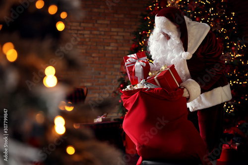 Santa Claus packing gifts into bag near Christmas tree photo