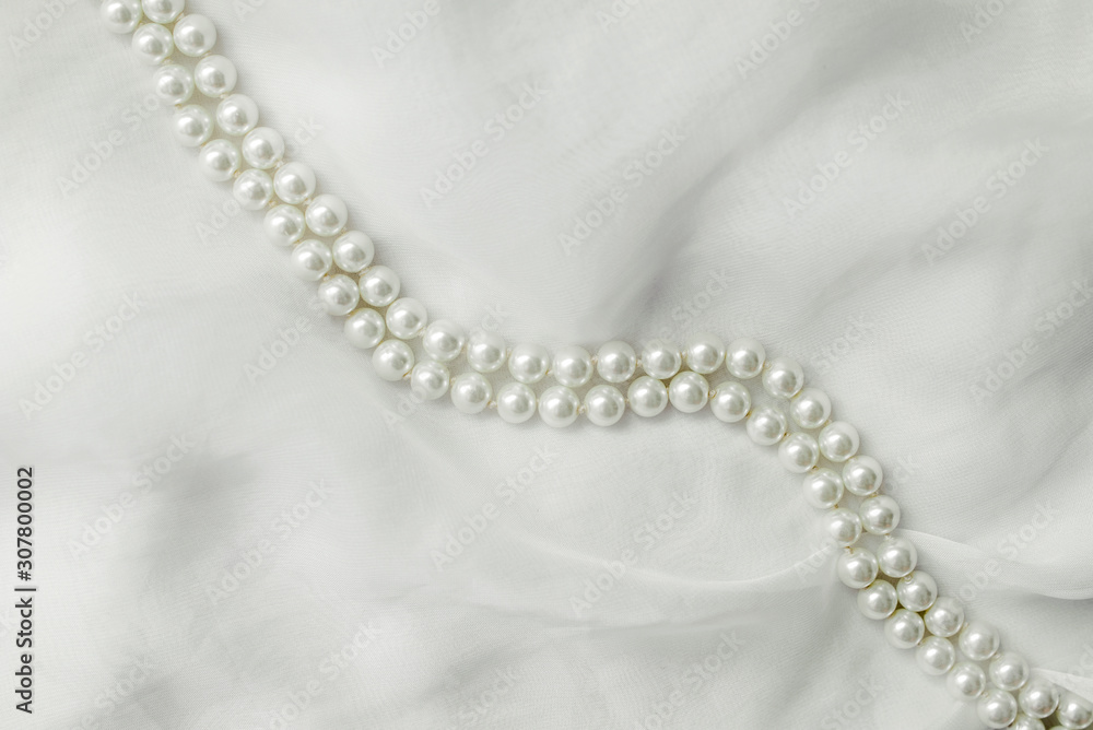 A necklace of pearls lies on a white cloth