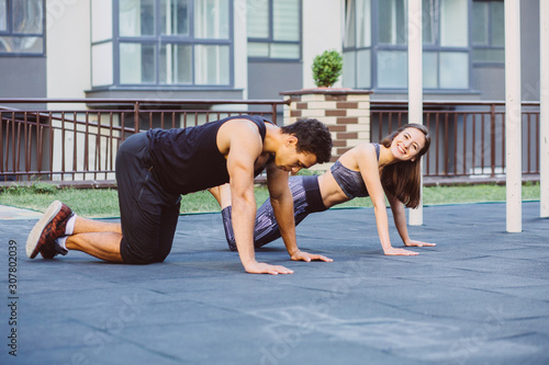 Low-angle view of a young fit woman and her partner smiling while practicing plank exercise during outdoor couple workout