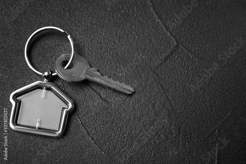 Key with trinket in shape of house on black stone background, top view and space for text. Real estate agent services © New Africa