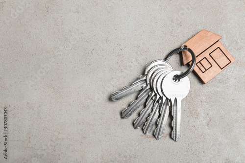 Keys with trinket in shape of house on grey stone background, top view and space for text. Real estate agent services photo