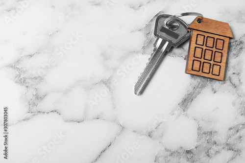 Key with trinket in shape of house on white marble background, top view and space for text. Real estate agent services © New Africa