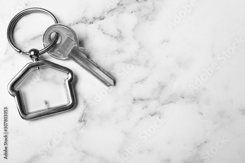 Key with trinket in shape of house on white marble background, top view and space for text. Real estate agent services © New Africa