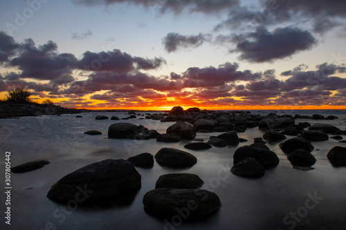 Vibrant colored cloudy winter sunset reflecting in ocean with endless horizon and dark ocean, silhouette of boulders laying in the foreground in shallow water at island of Gotland, Sweden