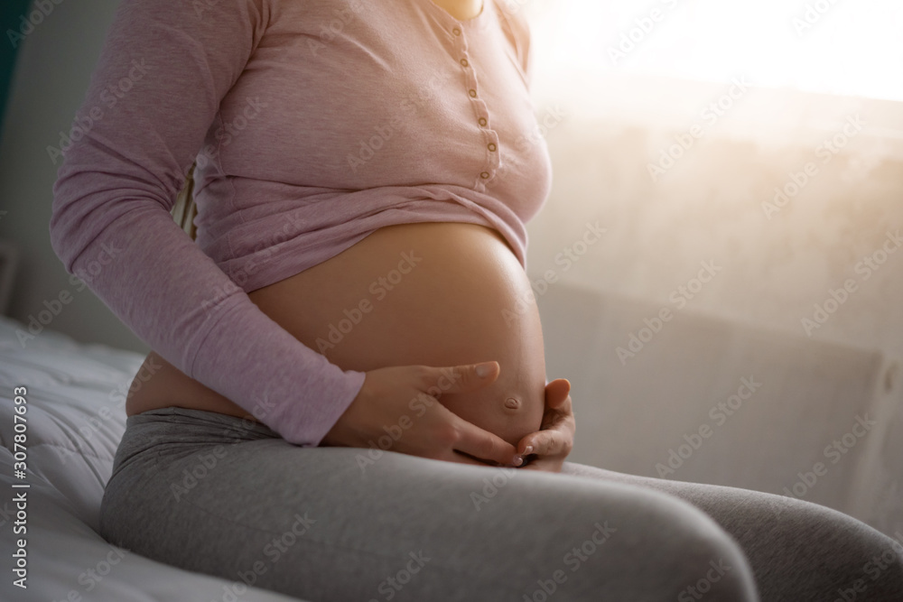 Pregnant woman holding her stomach and relaxing at home.