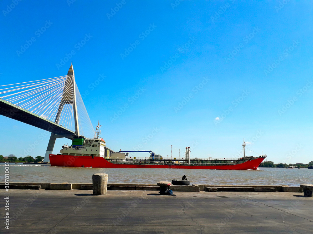 The jetty has a large red Large cargo ship Sailed through a large bridge Afternoon blue sky background The jetty has a large red Large cargo ship Sailed through a large bridge Afternoon blue sky background