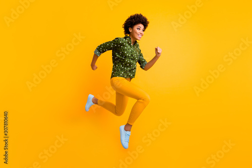 Full body photo of crazy dark skin curly lady jumping up high rushing fast discount shopping black friday prices wear green dotted shirt pants sneakers isolated yellow color background