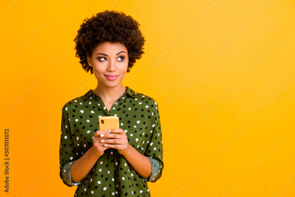 Photo of beautiful funny dark skin wavy lady hold telephone hands read good youth news look empty space advert wear green dotted shirt isolated yellow color background Photo of beautiful funny dark skin wavy lady hold telephone hands read good youth news look empty space advert wear green dotted shirt isolated yellow color background