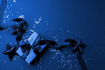 Christmas minimalistic and simple composition in mat trendy blue color. Christmas gift, toys decorations on black background. Flat lay, top view with copy space, sale, banner