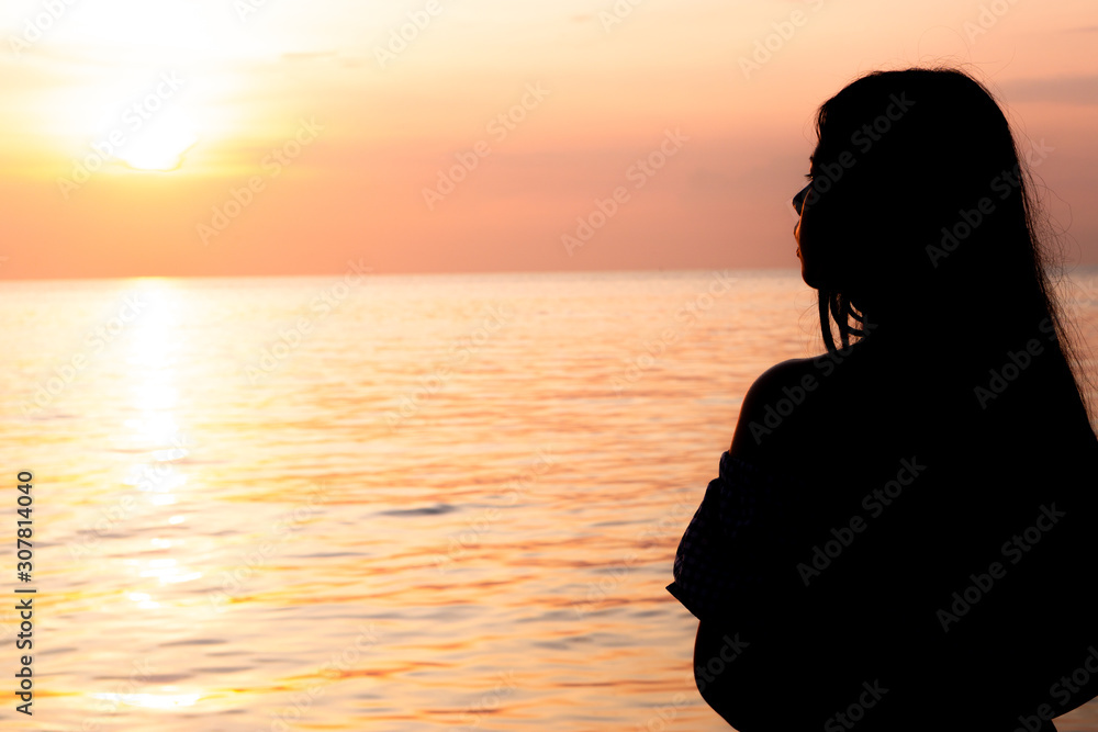 Silhouette of a lonely woman standing near the seashore and seeing the sunset. Depression, unhappy, stressed and anxiety disorder concept