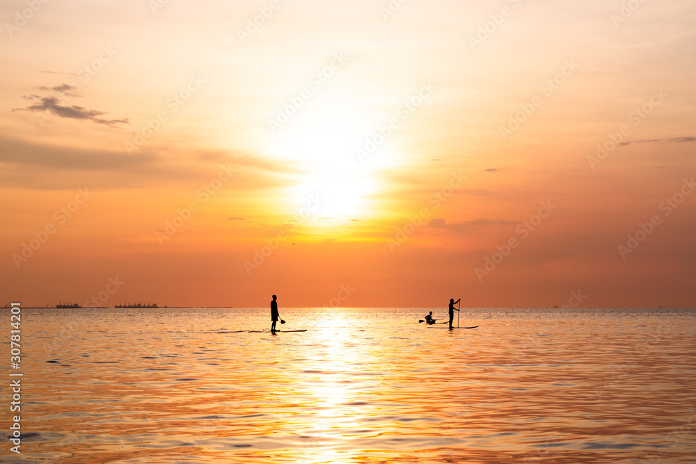 Silhouette of family playing the stand-up paddle board on the sea with beautiful summer sunset colors. Happy family concept.