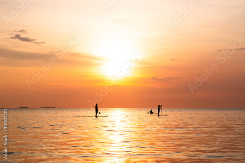Silhouette of family playing the stand-up paddle board on the sea with beautiful summer sunset colors. Happy family concept.