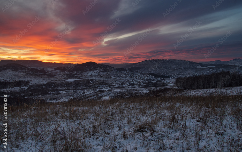 Winter dark sunset snow field on top of mountain slope on the background of  hills under colorful sky