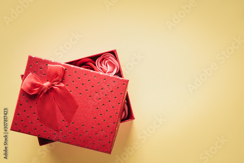 Top view gift box with buds of decorative roses inside the box on a yellow background with copy space