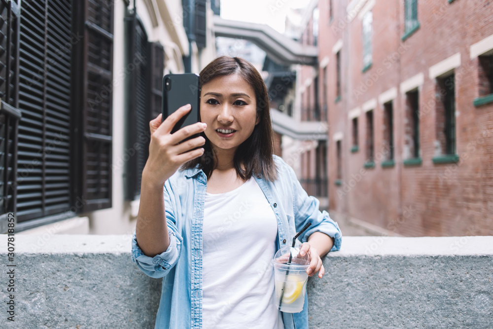 Glad ethnic woman with lemonade taking selfie