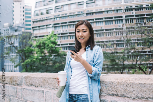 Asian woman with coffee and smartphone looking at camera