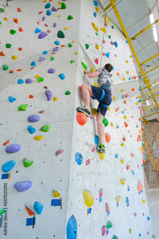 Sportsmen climbs boulder in a gym. A successful man climbing on climbing wall.