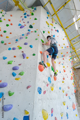 Sportsmen climbs boulder in a gym. A successful man climbing on climbing wall.