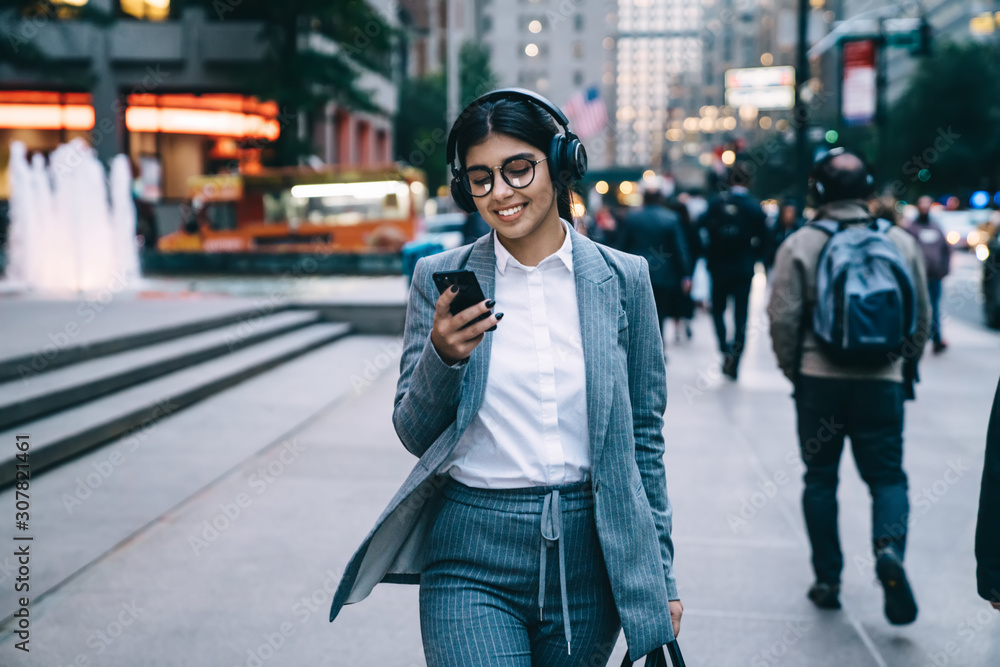Happy elegant businesswoman walking in downtown and using smartphone