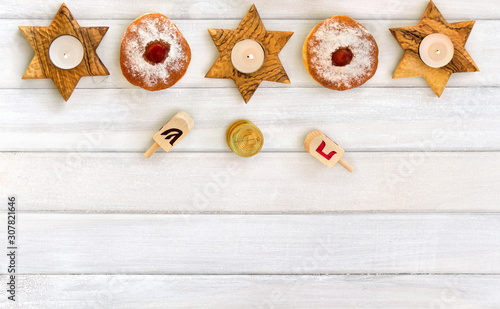 Wooden candlesticks in the shape of star, donut, golden chocolate coins and dreidels on background of white painted wooden planks with space for text. Jewish holiday Hanukkah. Top view, flat lay