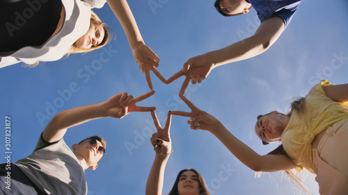 Friends make a star shape from their hands against a blue sky