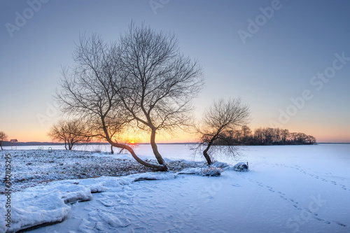 Winter landscape at sunset. Snowy nature Icy lake covered by snow and sun on horizon. Christmas time