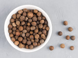 Allspice in a white bowl and peas on a gray concrete background