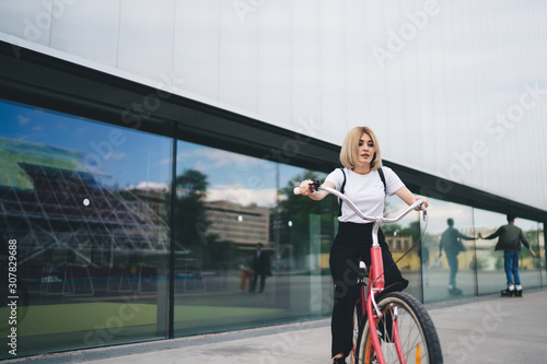 Young modern woman riding bicycle against mall