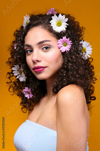 Portrait of happy beautiful woman with long bouncy curles hairstyle and professional make up on, posing over isolated yellow background. Fashion shot of young gorgeous female. Close up, copy space. © Evrymmnt