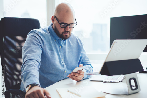 Focused adult man using smartphone at desk