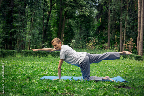 Young handsome man in sportswear does stretching in the park on the green grass. Prepare a warm-up for yoga or fitness classes.